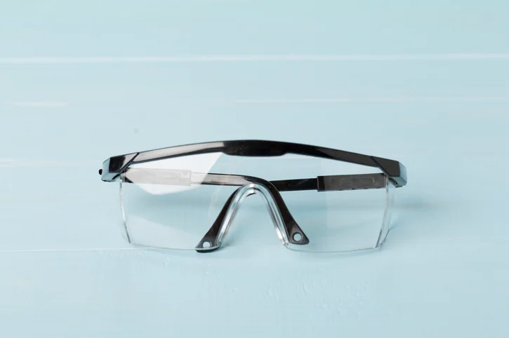 A pair of clear, acrylic safety glasses rests folded on a blue background.