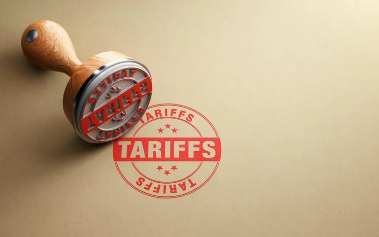 A red stamp that reads "tariffs" has been pressed onto a brown background. The stamper lays next to it.